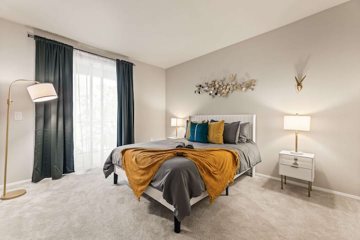 Spacious bedroom with a soft gray comforter, golden accent pillows, and a calming atmosphere.