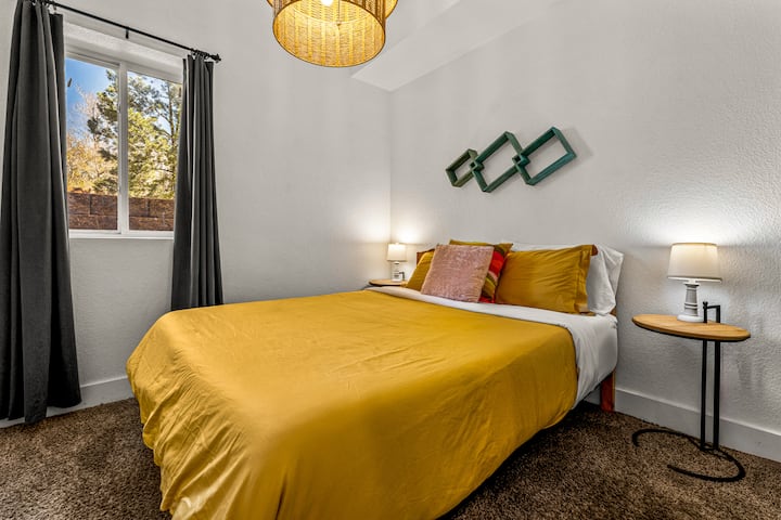 - Спална соба осветлена од сонцето со жолта постелнина од сенф и модерни акценти од средниот век
- Големиот прозорец го исполнува просторот со природна светлина и релаксирачки поглед
- Перниците на слоеви и висечките светилки создаваат удобно модерно место за одмор