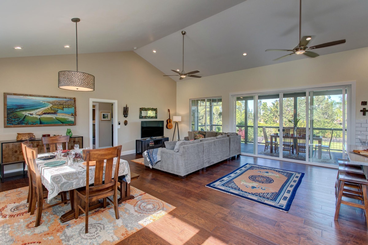 A spacious great room is showcased, featuring a dining area with a large table set for meals. A comfortable living area is furnished with a gray sofa, accent chairs, and a flat-screen TV. Sliding glass doors provide views of the outdoors, enhancing natural light.