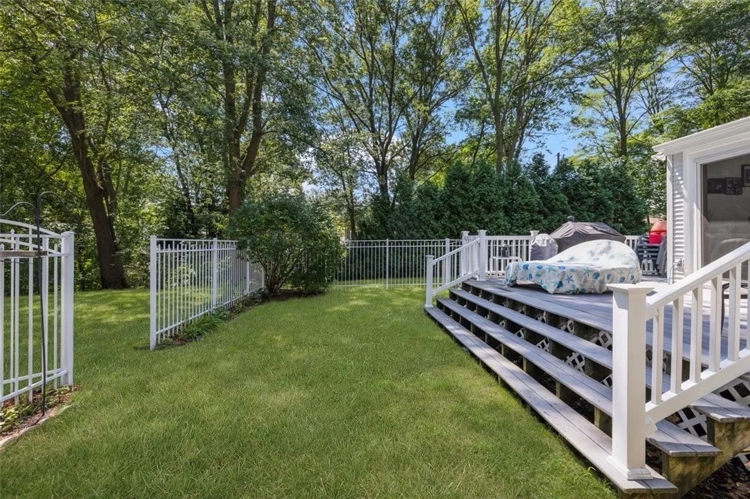 A spacious backyard is highlighted, featuring a securely fenced area and well-maintained grass. A wooden deck with steps is visible, equipped with outdoor seating. Lush trees and shrubs provide a natural backdrop, enhancing the outdoor space's serene and private feel.