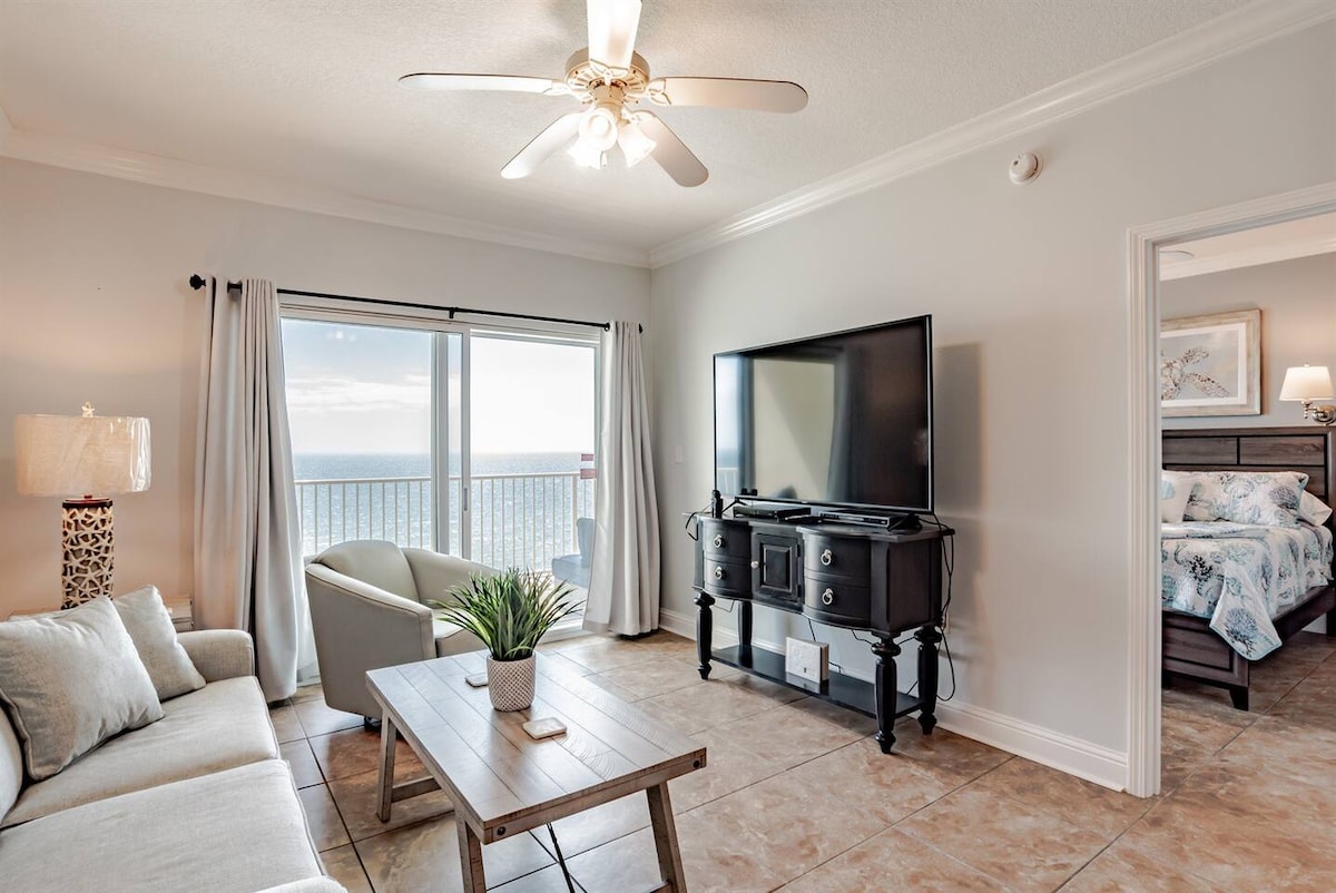 พื้นที่นั่งเล่นมีโซฟาปรับนอนสมาร์ททีวีจอแบนเครื่องนอนเก้าอี้นวมและประตูบานเลื่อนกระจกที่นำไปสู่ระเบียงส่วนตัวพร้อมวิวทะเลริมชายหาด