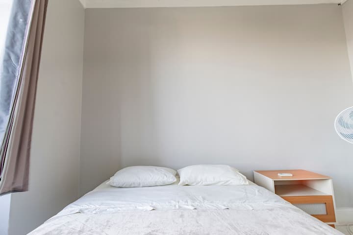 Segundo dormitorio compacto y cómodo con cama doble, ventilador de techo y mesa auxiliar naranja, ideal para que los niños o huéspedes adicionales descansen con tranquilidad.