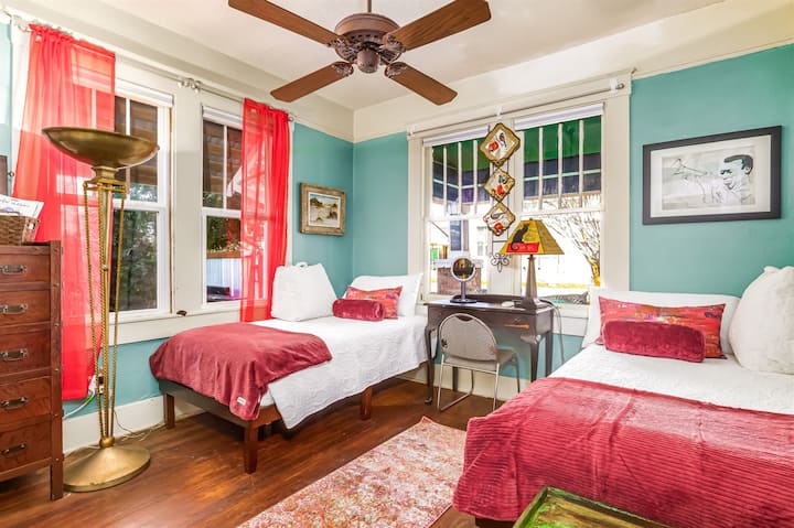 Bright and colorful twin bedroom ideal for teens or friends, with eclectic art and a desk overlooking the historic East Hill neighborhood.