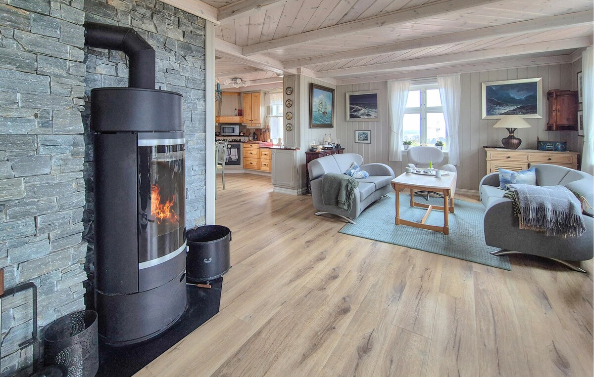 A spacious living area features a stone fireplace with a visible flame, providing warmth. Two couches and a coffee table are arranged invitingly around a light area rug. Large windows allow natural light to fill the room, complemented by artwork adorning the walls.