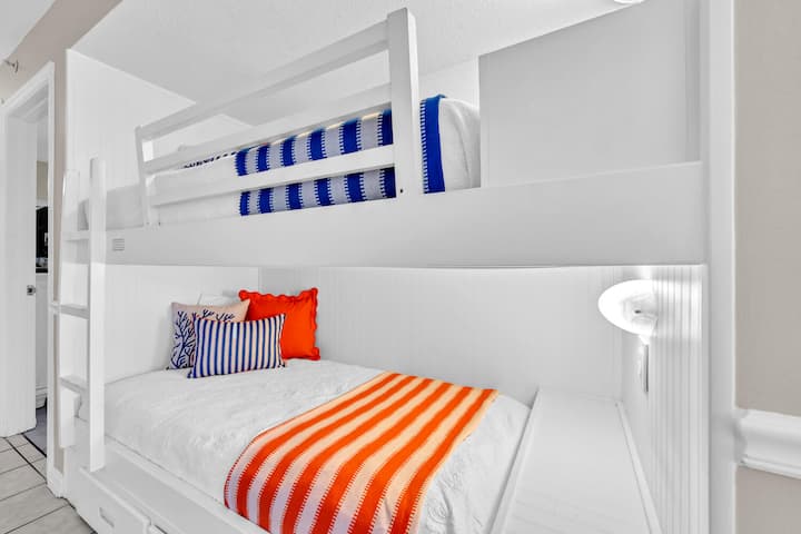 Sus literas de color blanco brillante crean el refugio acogedor perfecto, con sábanas a rayas alegres y prácticas lámparas de lectura para los cuentos antes de dormir.