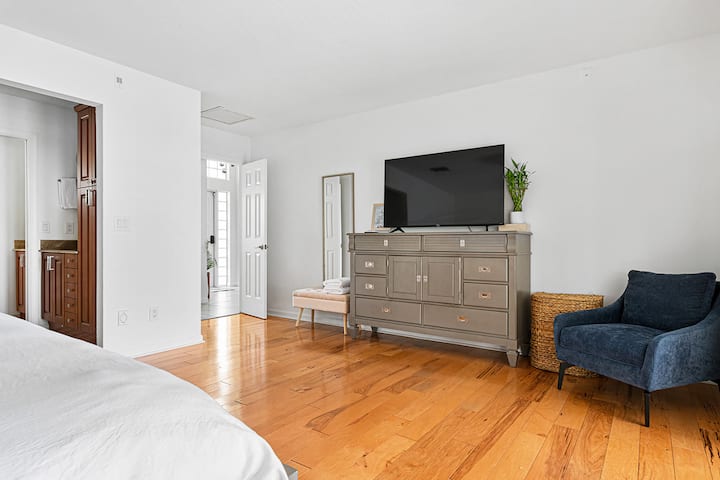 Une chambre spacieuse chambre avec un plancher de bois franc, une chaise confortable et une télévision, créant un espace relaxant et fonctionnel.