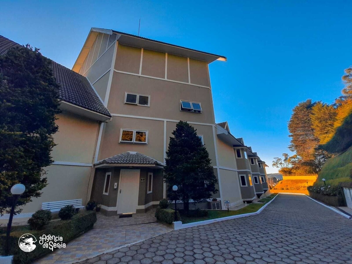 A multi-story building is set within a peaceful environment, featuring a light-colored exterior and multiple windows. The pathway is lined with manicured greenery and outdoor lights, inviting guests to explore the serene surroundings.