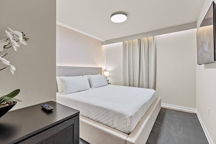 Esta acogedora recámara cuenta con una cama lujosa y bien tendida, enmarcada por cortinas suaves y fluidas que difunden la luz con delicadeza. Una elegante mesita de noche y obras de arte contemporáneas agregan toques modernos, creando una atmósfera relajante para noches de descanso.
