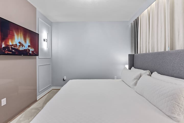 Esta acogedora recámara cuenta con una lujosa cabecera tapizada en gris para darle un toque de sofisticación, iluminación suave, paredes en un relajante tono azul y un elegante televisor montado en la pared, lo que crea un espacio acogedor para relajarte después de tus aventuras.