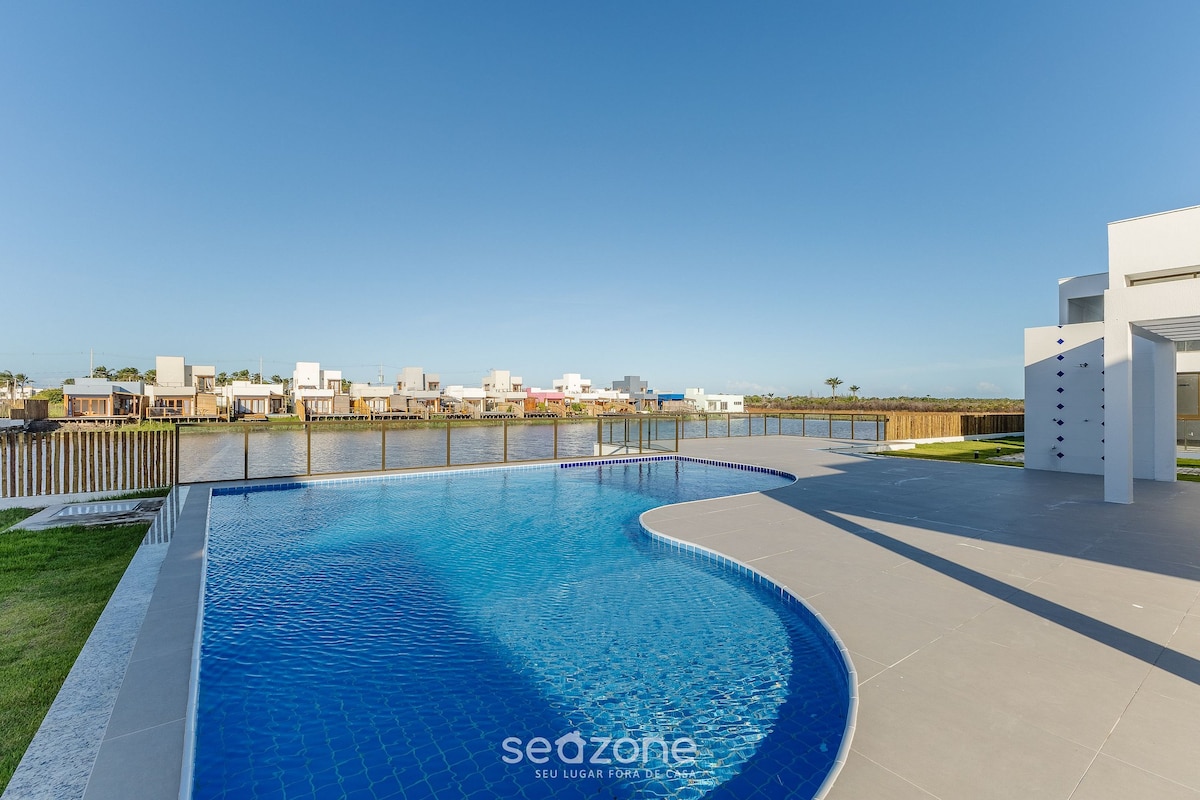 A spacious swimming pool is situated beside a well-kept lawn, offering views of surrounding modern architecture. The water is a deep blue, reflecting the clear sky. The patio area provides ample space for relaxation and outdoor activities.
