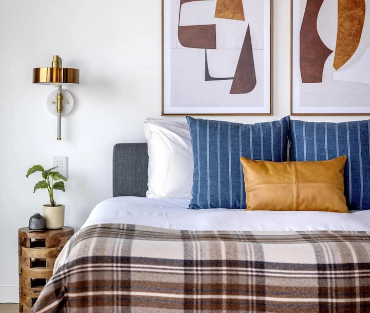 Ზოლებიანი ბალიშები და საბანი საწოლზე ჩარჩოში ჩასმული კედლის ხელოვნებით