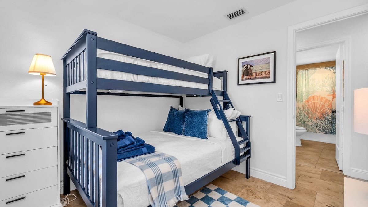 Este acogedor segundo dormitorio cuenta con una elegante litera doble azul marino, perfecta para niños, adolescentes o invitados adicionales. Con ropa de cama de felpa, una alfombra a cuadros y alegres detalles costeros, es un espacio divertido y funcional que encantará a toda la familia.