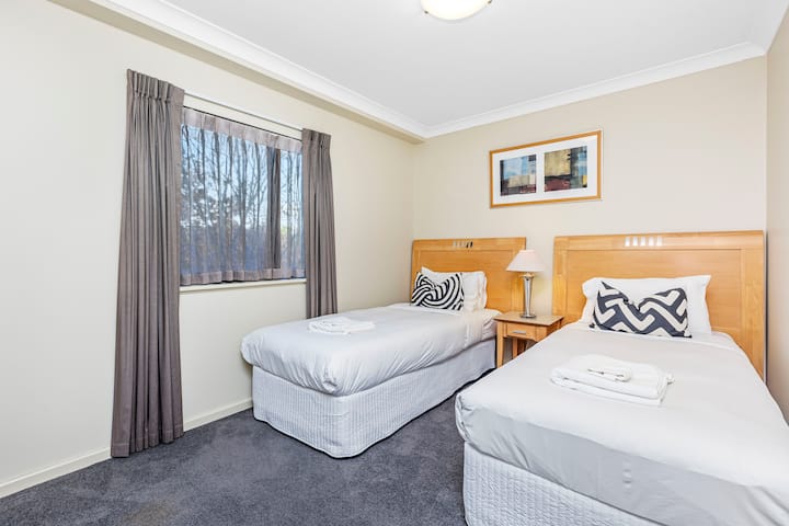 Karibu kwenye chumba cha kulala chenye starehe na utulivu, kilichopangwa kikamilifu na vitanda viwili vya mtu mmoja, kila kimoja kimepambwa kwa mashuka meupe na mito maridadi. Meza ya kando ya kitanda iliyo na taa inatoa urahisi. 