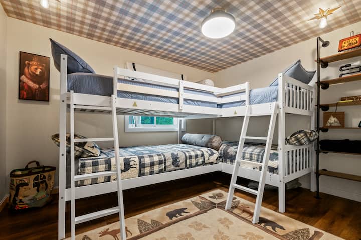 Ultimate bunk room featuring 4 twin beds, Roku TV, industrial pipe-style clothing rack, standalone fan, fun gallery wall, and Pack ’n Play stored underneath. Perfect for kids, teens, and adults during family getaways in the White Mountains.