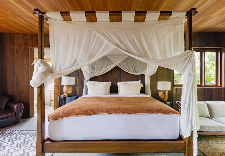 Cama con dosel de cuatro postes con cortinas blancas.