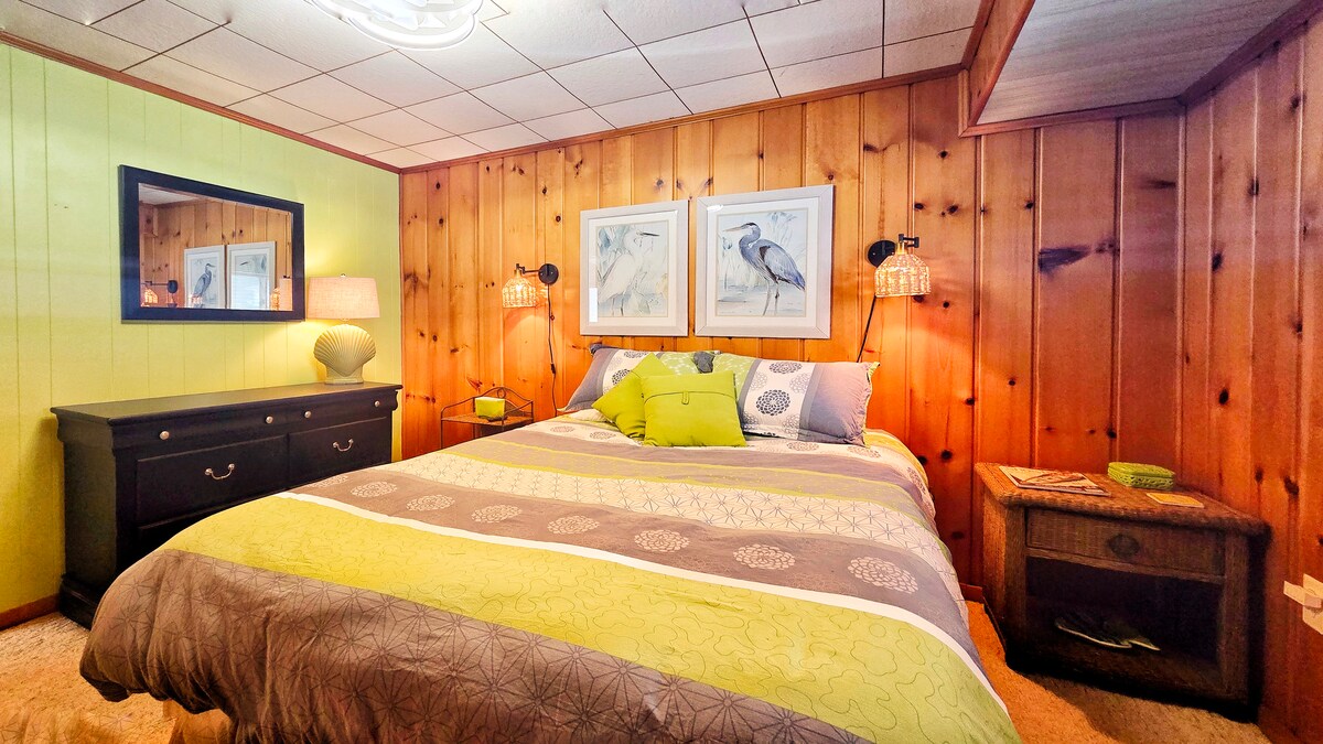 Cozy wood-paneled bedroom with queen bed, sconces, and dresser.