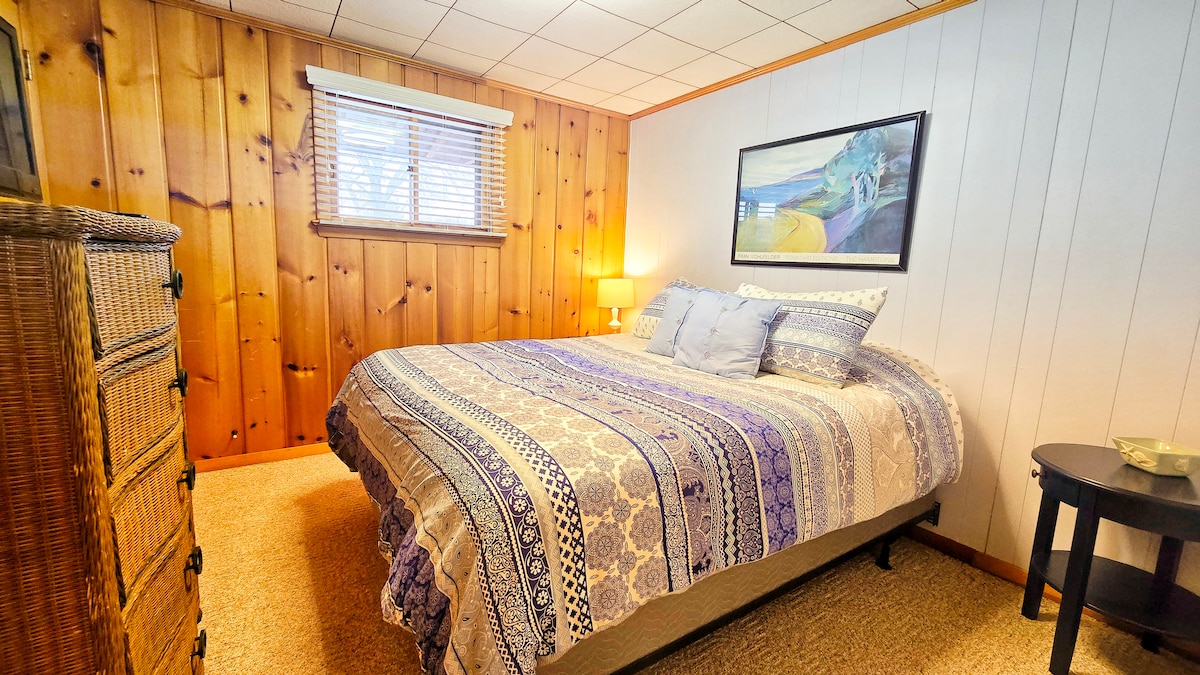 Cozy wood-paneled bedroom with plush queen bed and warm glow