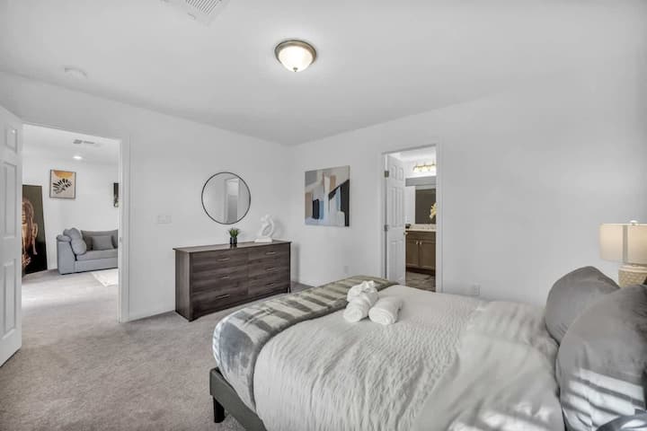 A modern bedroom featuring a cozy queen-sized bed with crisp linens, elegant lamps, a stylish dresser, a minimalist mirror, and calming artwork, offering a tranquil and inviting retreat.