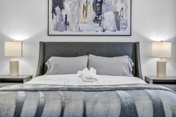 A stylish bedroom with a chic gray upholstered queen-sized bed, soft gray linens, cozy lamps on matching nightstands, and a modern abstract art piece, creating a calm and inviting atmosphere.