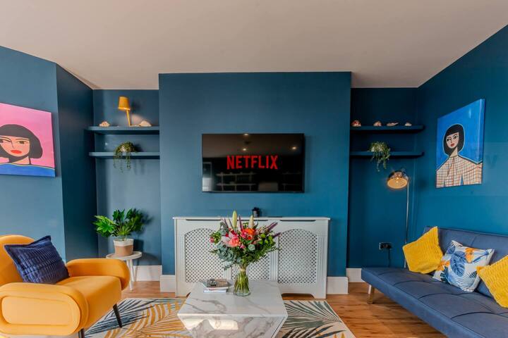  Dnevni boravak / salon
Uživajte u panoramskom pogledu na more u ovom živopisnom prostoru uređenom u stilu dizajna. Zbog zidova u tamnoplavoj boji, umjetničkih djela, elegantnih starih elemenata i visokih prozora s okvirom, dnevni boravak poziva vas da se opustite u udobnosti. Uronite u plišane sjedeće garniture