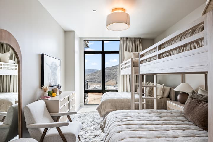 - Bunk room featuring two full beds with twin bunks overhead  
- Large window with natural light and scenic mountain view  
- Modern design with cozy seating and stylish accents inside