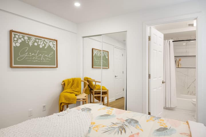 Zgjohu nga qetësia me lule – Një dhomë gjumi e ndritshme me një art muri, hedhje mustardë të verdhë dhe një banjë mermeri brenda në suitë.