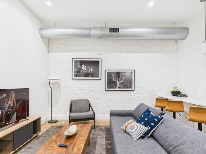 Ambient ndenjjeje me koncept të hapur me mobilie të rehatshme, televizor inteligjent dhe divan për fjetje.