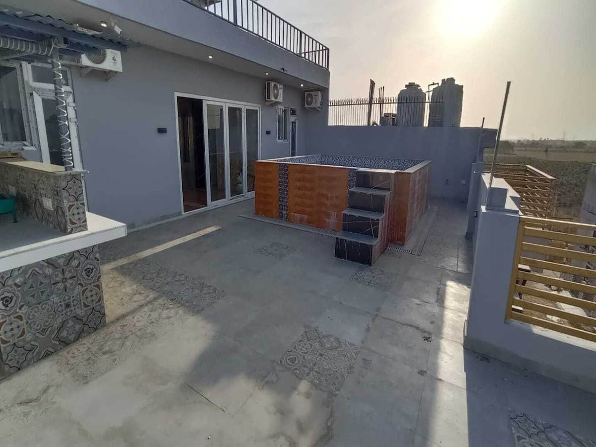 An exterior terrace area features a spacious layout with an outdoor seating arrangement. A small plunge pool is set against a backdrop of city buildings. The terrace is bordered by decorative tiled walls and offers expansive views of the surrounding landscape.