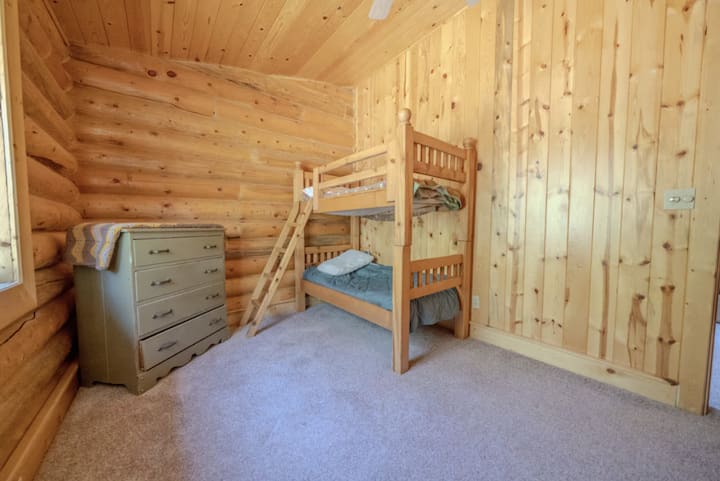 Charmante kinderkamer met stevige stapelbedden ontworpen voor kinderen. De warme houten muren creëren een gezellige omgeving, perfect voor spel en rust. Een dressoir voegt opbergruimte toe, waardoor het een ideale plek is voor jonge avonturiers om te ontspannen na een dag vol plezier