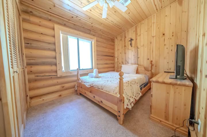 Uitnodigende slaapkamer met een queensize bed met zacht linnengoed en een gezellige sfeer. De warme houten lambrisering en het grote raam zorgen voor natuurlijk licht. Deze kamer is perfect voor een rustgevend verblijf en biedt een serene retraite met moderne voorzieningen voor jouw comfort.