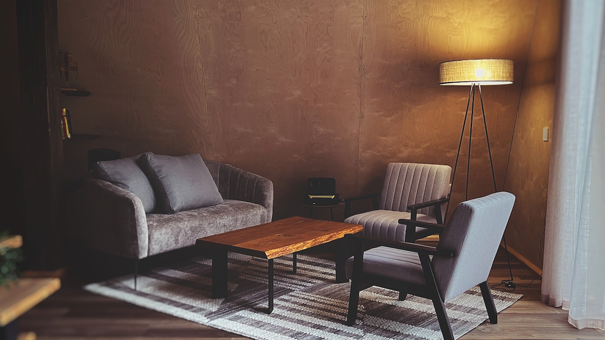 A cozy seating area is highlighted by a comfortable sofa and two armchairs, complemented by a wooden coffee table. Soft lighting from a floor lamp creates a warm ambiance, while a textured rug adds an inviting touch to the wooden floor.