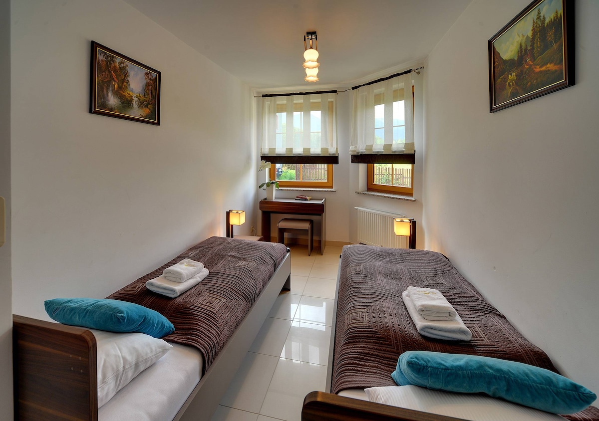 Një dhomë gjumi dyshe me dy krevate të veshur me mbulesa kafe dhe jastëkë blu të hapur. Një komodinë e vogël i ndan ato dhe mbi çdo krevat ka art muri.