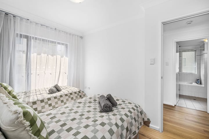 Svijetla i udobna spavaća soba s dva jednostruka kreveta s kariranom posteljinom i mekanim prekrivačima. Veliki prozori s prozirnim zavjesama omogućuju da prostor bude ispunjen prirodnim svjetlom. 