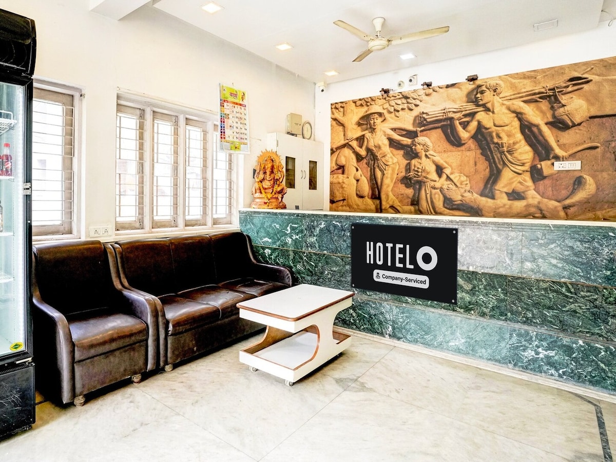 A welcoming reception area features a brown leather sofa set and a marble table. The wall displays a unique mural depicting a historical scene, complemented by natural light filtering through window panes. A reception desk is set against a green marble backdrop, offering a warm entry point.