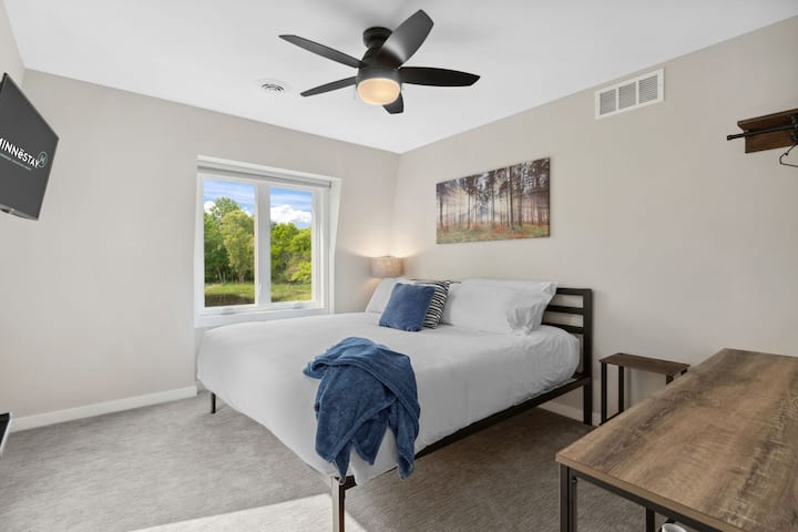 Drift off to sleep in your tranquil bedroom with crisp linens, peaceful forest artwork, and natural light streaming through windows overlooking lush greenery.