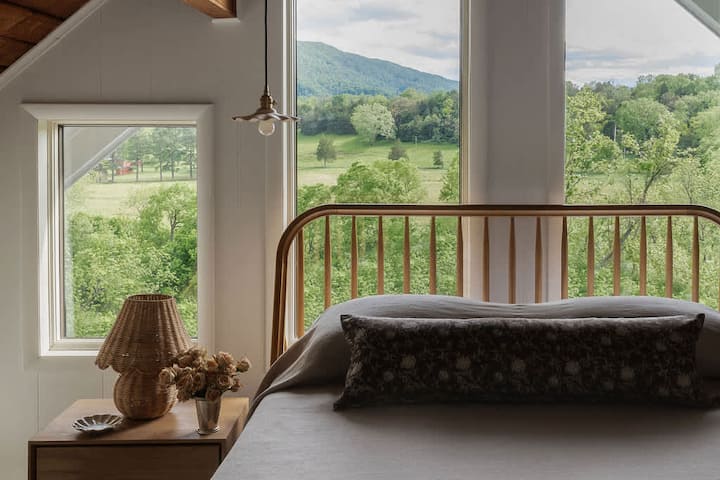 Wake up to stunning mountain views from the comfort of this upstairs queen bedroom, featuring a classic iron bed and warm, natural light.