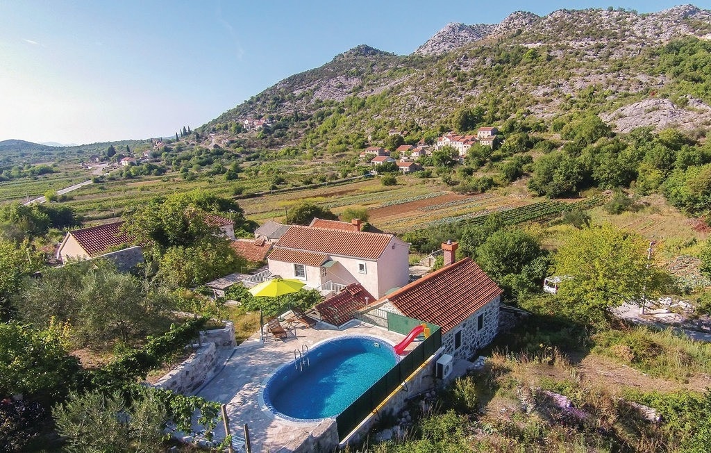 Aerial view of a spacious rural property featuring a private swimming pool surrounded by landscaped gardens. The house is complemented by outdoor seating under a bright yellow canopy. Rolling hills and vineyards create a scenic backdrop, enhancing the countryside ambiance.