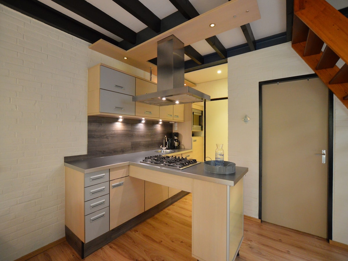 A well-appointed kitchen is featured, equipped with modern appliances including a gas stove and dishwasher. The light wood cabinetry complements the spacious countertop. A unique ceiling design with exposed beams adds character to the area. Natural light is enhanced by the warm-toned wood flooring.