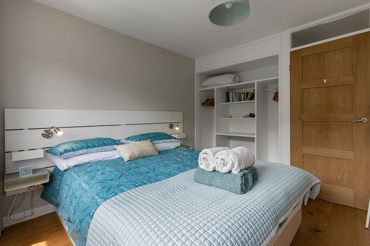 Mirna i elegantna dvokrevetna spavaća soba s čistom garderobom otvorenog tipa i puno prirodnog svjetla.