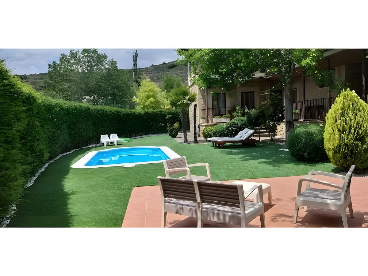 The outdoor area features a private pool surrounded by lush greenery and well-manicured hedges. A sunbathing area is highlighted with lounge chairs and a sleek chaise, offering a serene environment for relaxation. The space reflects a calm and inviting atmosphere, ideal for enjoying warm days.