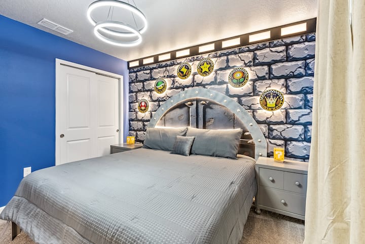 Experience a cozy bedroom with a stunning blue accent wall and decorative shields, paired with soft gray bedding and chic nightstands. Modern lighting adds to the decor, creating a warm and inviting atmosphere for your stay.