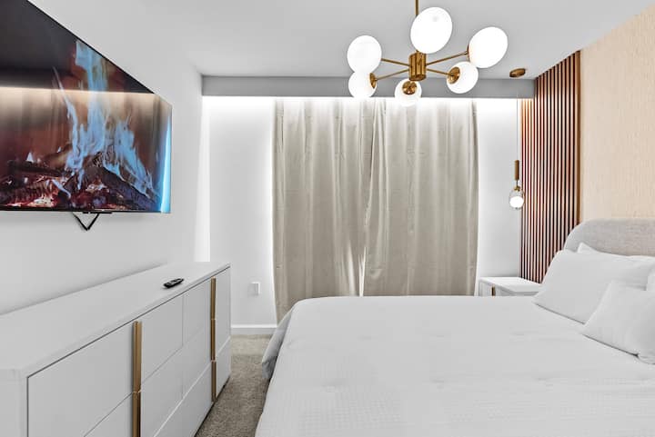 Experience a stylish bedroom with a cozy bed and a modern light fixture for a touch of elegance. Soft neutral tones create a serene atmosphere, while a large window with elegant curtains lets in beautiful natural light.