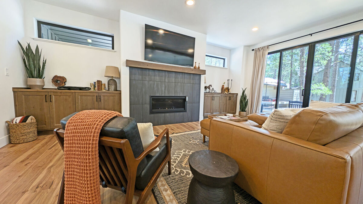 A spacious living area features a modern fireplace with a sleek, dark surround. Large windows allow natural light to fill the room, complemented by a cozy seating arrangement that includes a leather sofa and stylish accent chairs. Decorative elements enhance the inviting atmosphere.