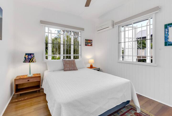 El dormitorio principal combina lino blanco fresco con artículos coloridos e iluminación suave, creando un refugio tranquilo enfriado por aire acondicionado y un ventilador de techo.