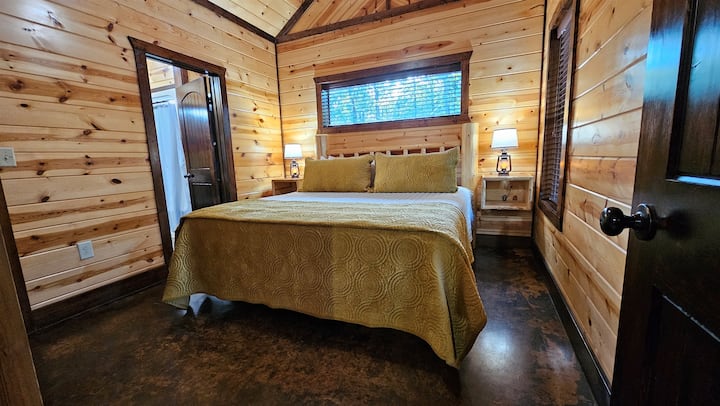 Sunlit King bedroom with log-style headboard, lantern nightstand lamps, and tree-view window — warm and ready to unwind in