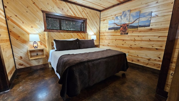 King bedroom with longhorn canvas wall art, lantern lamps, and warm knotty pine walls — Western character built right in
