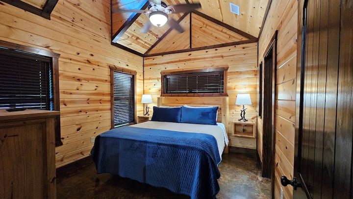 King bedroom with vaulted knotty pine ceiling, ceiling fan, antler-base nightstand lamps — cozy and dark enough for a solid night's sleep