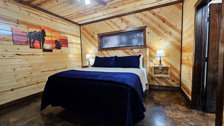 King bedroom with log-frame platform bed, dual nightstand lamps, and knotty-pine vaulted walls — built for a good night's sleep