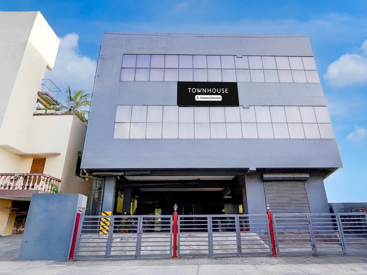 The exterior of a modern multi-story building is displayed, featuring large windows that allow for natural light. The entrance is secured by a gate, emphasizing a contemporary design. The building is set against a clear blue sky, contributing to a welcoming appearance.