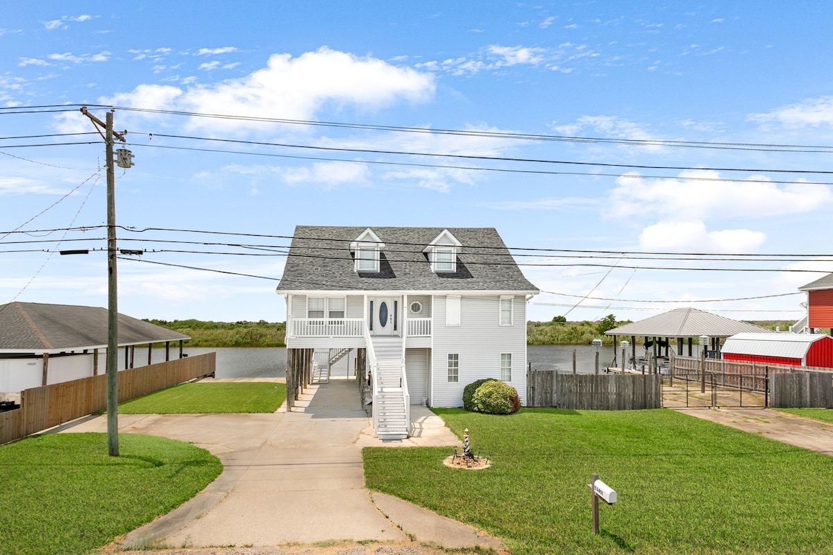 A two-story home with a traditional design is situated on a spacious lot. The exterior features a combination of white siding and a grey roof. Surrounding green lawns and a tranquil water view enhance the peaceful setting of this Slidell retreat.